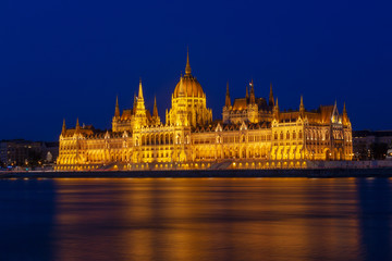 Fototapeta na wymiar The Hungarian Parliament Building, a notable landmark of Hungary in Budapest. View of the main facade illuminated above the Danube river. Long exposure at a blue hour after sunset.
