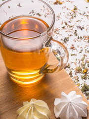 Closeup view of glass mug with hot herbal tea with crispy meringues and dried leaves and petals in the background