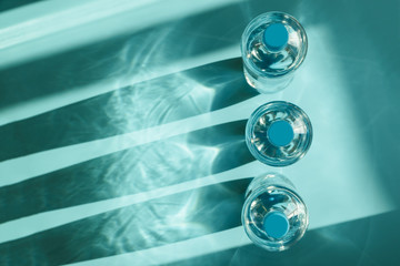 Three bottles of water with reflecting shadows on blue background.  Healthy food concept. Top view. Copy space