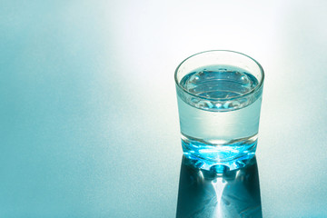 Glass of water with reflecting shadows on blue background.  Healthy food concept. Top view. Copy space