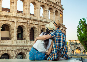 Obraz na płótnie Canvas Lovely couple of tourist sitting on a wall at Colosseum hugging. Rome, Italy