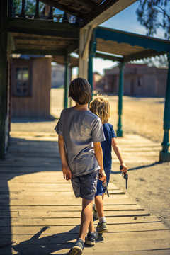 Two boys holding gun replica, walking in a western old town