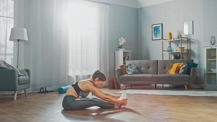 Beautiful Confident Fitness Girl in an Athletic Workout Clothes Doing Stretching Exercises in Her Bright and Spacious Living Room with Cozy Minimalistic Interior.