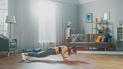 Strong and Fit Beautiful Girl in a Grey Athletic Outfit Energetically Exercising in Her Bright and Spacious Living Room with Minimalistic Interior.