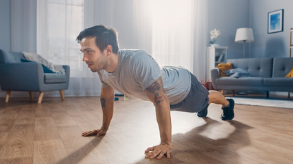 Muscular Athletic Fit Man in T-shirt and Shorts is Doing Push Up Exercises at Home in His Spacious and Bright Apartment with Minimalistic Interior.