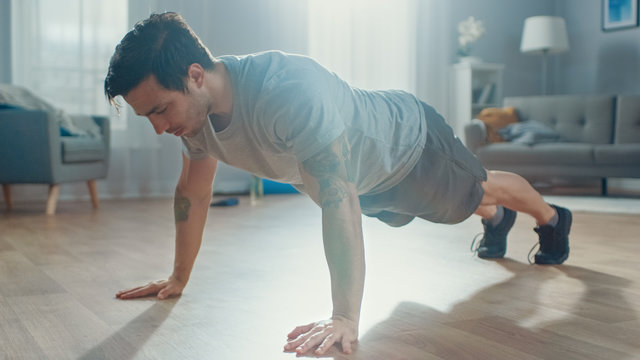 Strong Athletic Fit Man In T-shirt And Shorts Is Doing Push Up Exercises At Home In His Spacious And Bright Living Room With Minimalistic Interior.