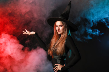 Fototapeta premium Beautiful woman dressed as witch for Halloween on dark background
