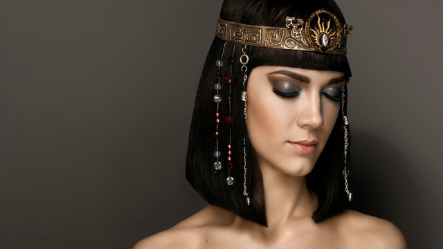 Glamorous closeup portrait of beautiful sexy stylish brunette young woman with bright makeup with perfect clean skin with gold jewelery. High fashion look. Beautiful Girl's Face Hairstyle Cleopatra 