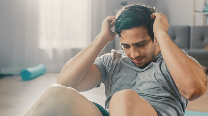 Strong Athletic Fit Man in T-shirt and Shorts is Doing Abdominal Crunch Workout at Home in His Spacious and Bright Living Room with Minimalistic Interior.