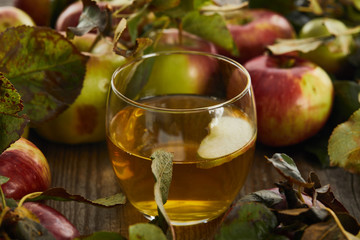 glass of fresh cider near apples on wooden surface