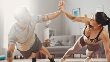 Strong and Beautiful Athletic Fitness Couple in Workout Clothes Doing Push Up Exercises and Giving Each Other a High Five in Their Bright and Spacious Living Room with Minimalistic Interior.