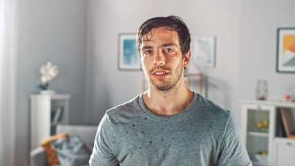 Sweating Muscular Athletic Fit Man in Grey Outfit is Posing After a Workout at Home in His Spacious and Sunny Living Room with Minimalistic Interior.