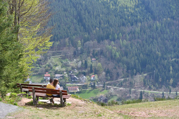 Bad Wildbad, Germany - April 22, 2019: A guy and a girl are sitting on a bench and admiring, the beautiful European landscape. Romantic meeting of a guy and a girl on top of a mountain