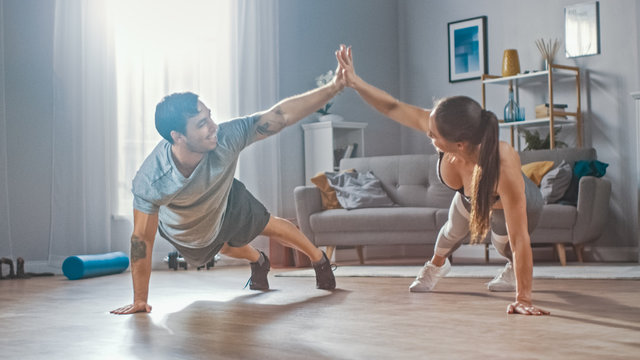 Strong and Beautiful Athletic Fitness Couple in Workout Clothes Doing Push Up Exercises and Giving Each Other a High Five in Their Bright and Spacious Living Room with Minimalistic Interior.