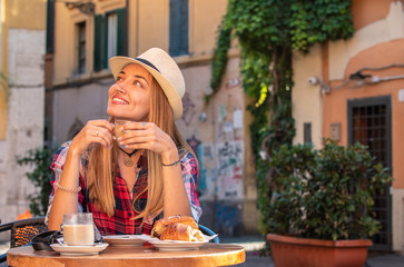 Young blonde woman with blue eyes having breakfast in typical Italian bar outside in historical...