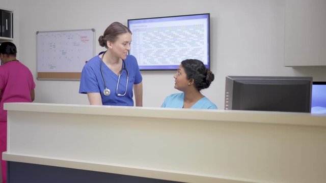 Three nurses at nursing station, two talk, camera move left right, stethoscope