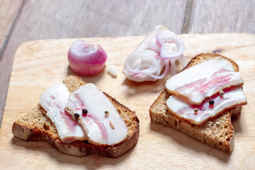 Lard sandwich with black bread and onions on a wooden board.