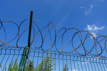 Coils of razor wire on a metal fence in the background of the blue sky with clouds