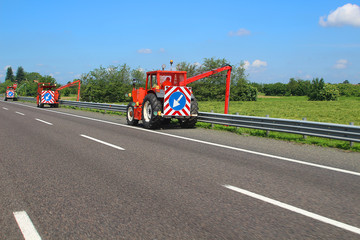 Several tractors mowing grass along the highway