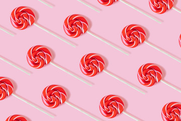 Bright spectacular background of red round lollipops on a pastel pink background. Stilysh pattern. Minimalism, flat lay, top view, design.