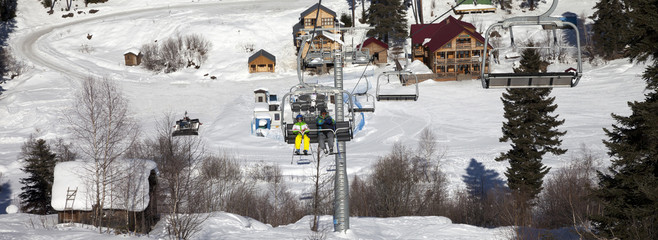 Skiers on chair-lift at ski resort in sun winter day