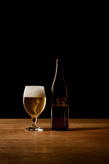 glass and bottle of beer on wooden table isolated on black
