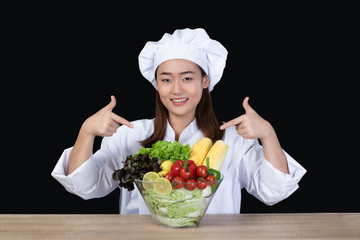 Portrait of a young beautiful Asian woman chef smiling and preparing ingredients for meal or salad. She was happy and confident .Half figured, Isolated and studio lighting on black background.