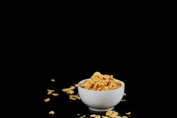 white bowl with cornflakes and scattered pieces isolated on black