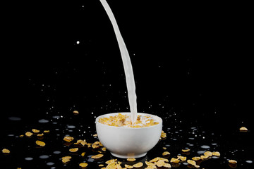 white bowl with cornflakes with milk stream isolated on black