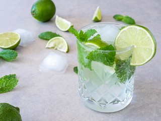 A mojito cocktail made from fresh mint and lime in a cut glass tumbler against a pale background