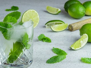 A mojito cocktail made from fresh mint and lime in a cut glass tumbler against a pale background