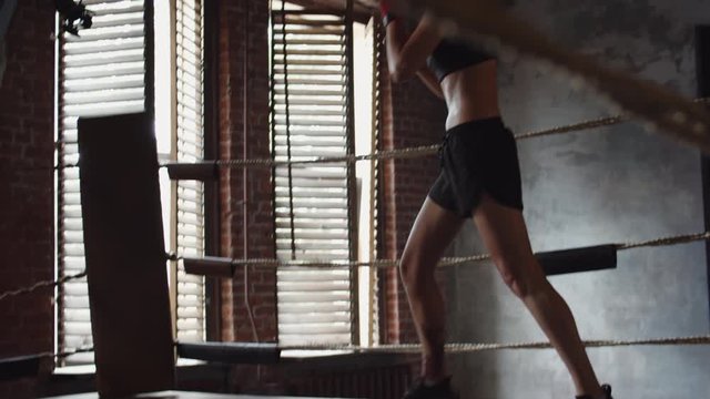 Tilt up of Caucasian young female fighter wearing racerback tank top and shorts training punches inside boxing ring