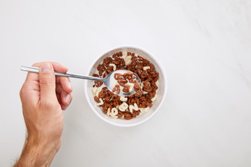 cropped image of man taking cereal with spoon from bowl on marble surface