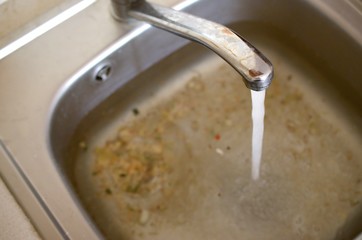 Stainless steel sink plug hole close up full of water and particles of food