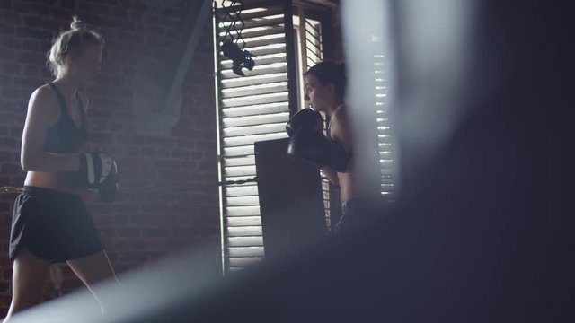 Medium shot of two muscular female kickboxers in gloves having sparring fight in boxing studio