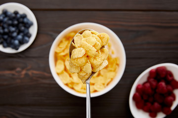 top view of spoon with cornflakes above wooden surface with berries
