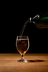 beer pouring from bottle in glass on wooden table isolated on black