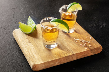 Golden tequila shots with lime slices and salt rims on a black background