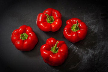 Fresh four red peppers on a black background in the center of the frame.