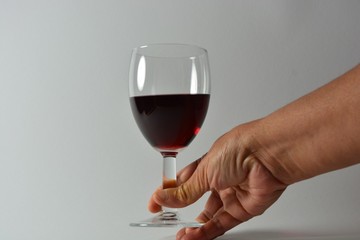 A person holding a glass of red wine in front of a white background