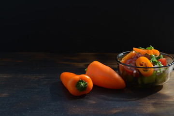 Orange peppers on a burned wooden table next to a small bowl of salad
