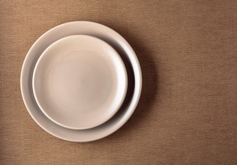 Empty ceramic round beige plate on a beige tablecloth.