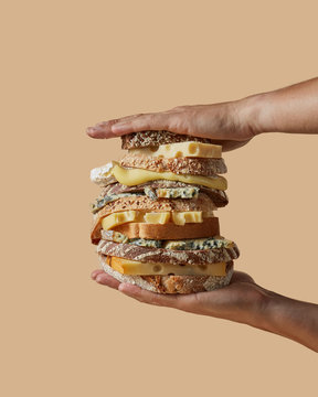 The hands of the men hold a large sandwich made from different cheese and different healthy bread with sesame seeds on a light brown background with copy space.