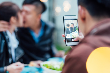 Young man taking photos of a couple kissing in a dinner