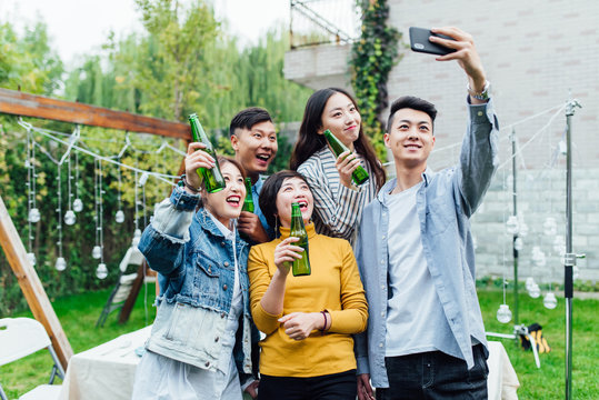 A group of young friends making selfie with beers in a backyard party