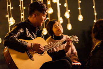 Group smiling friends with acoustic guitar singing and drinking beer