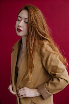 Redhead pretty woman button her coat by dark red background