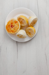 Squeezed lemons close-up on a white plate on a background of gray wooden table. The preparation of lemonade.
