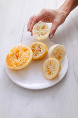 Squeezed lemons close-up on a white plate on a background of gray wooden table. The preparation of lemonade.