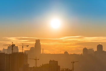 Panoramic view of sunset in the city with silhouette of buildings and industrial cranes